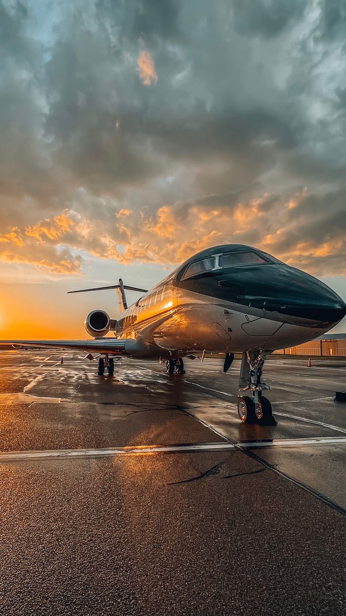 Services A sleek private jet parked on a wet tarmac during a colorful sunset at an airport.